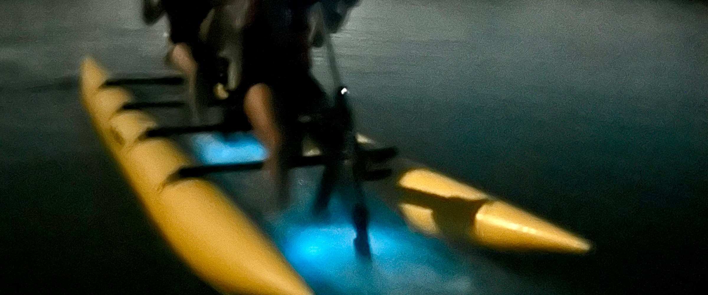 Blurred image of two people on a kayak at night with glowing blue light.