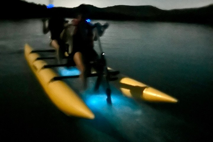 Blurry night image of people in a kayak with blue lights on a calm lake.