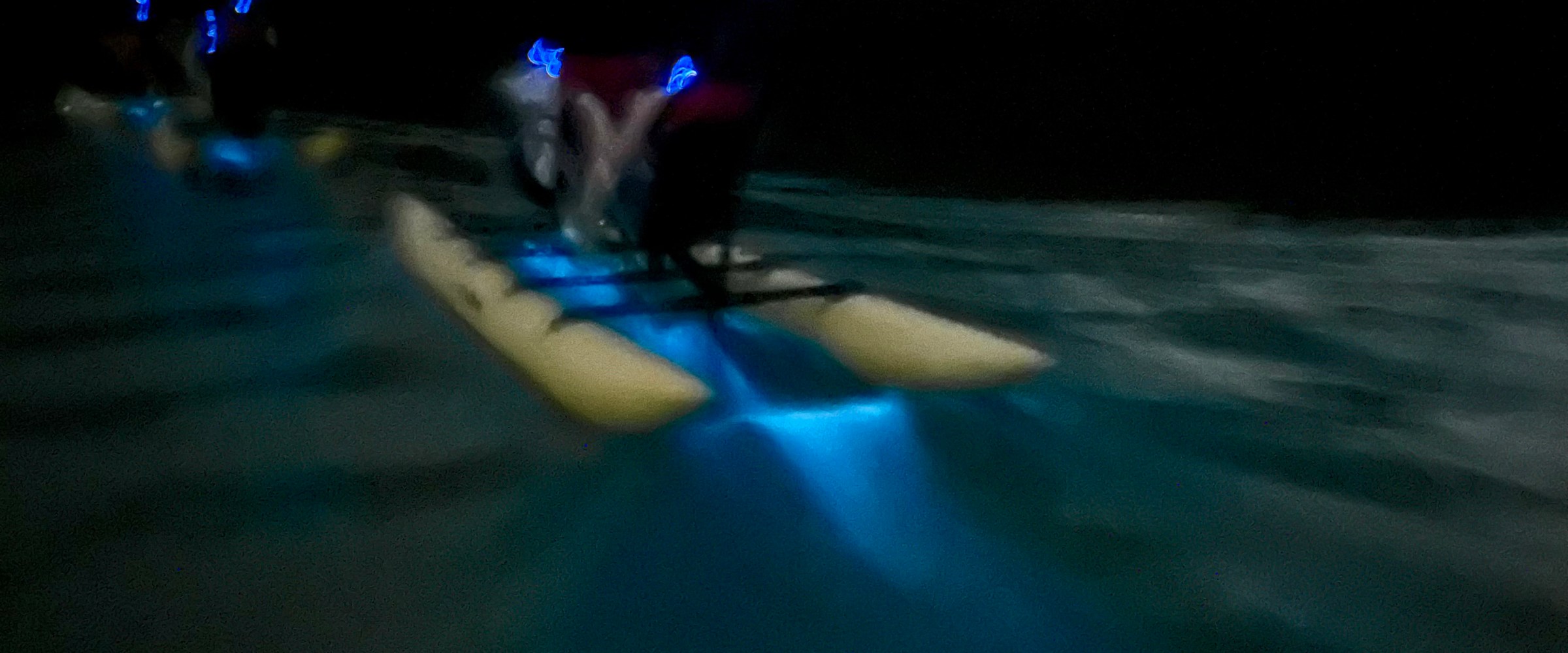 Shadowy figures kayaking at night with blue lights on water.