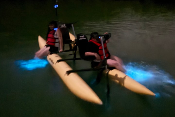 Two people in a kayak with blue bioluminescent water at night.