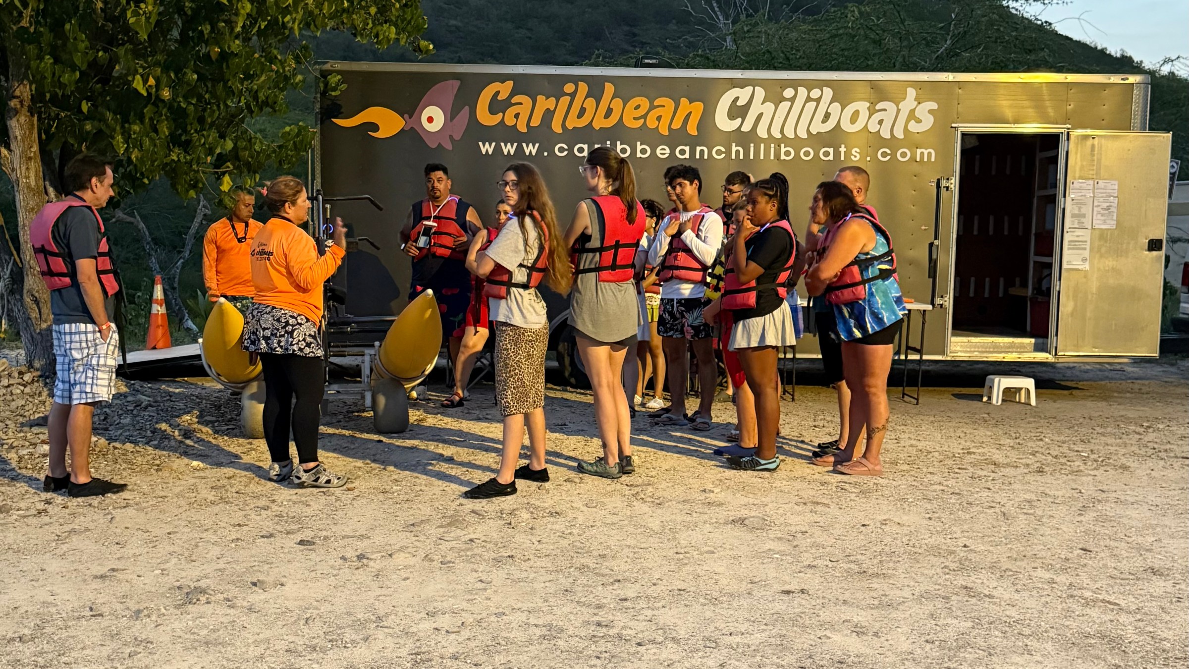 Group in life vests gathered near a 'Caribbean Chillboats' trailer for instructions.