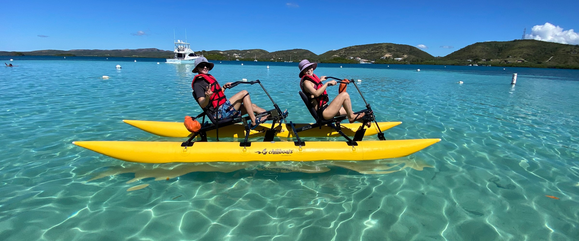 Two people riding a yellow water bike on clear blue ocean under a sunny sky.