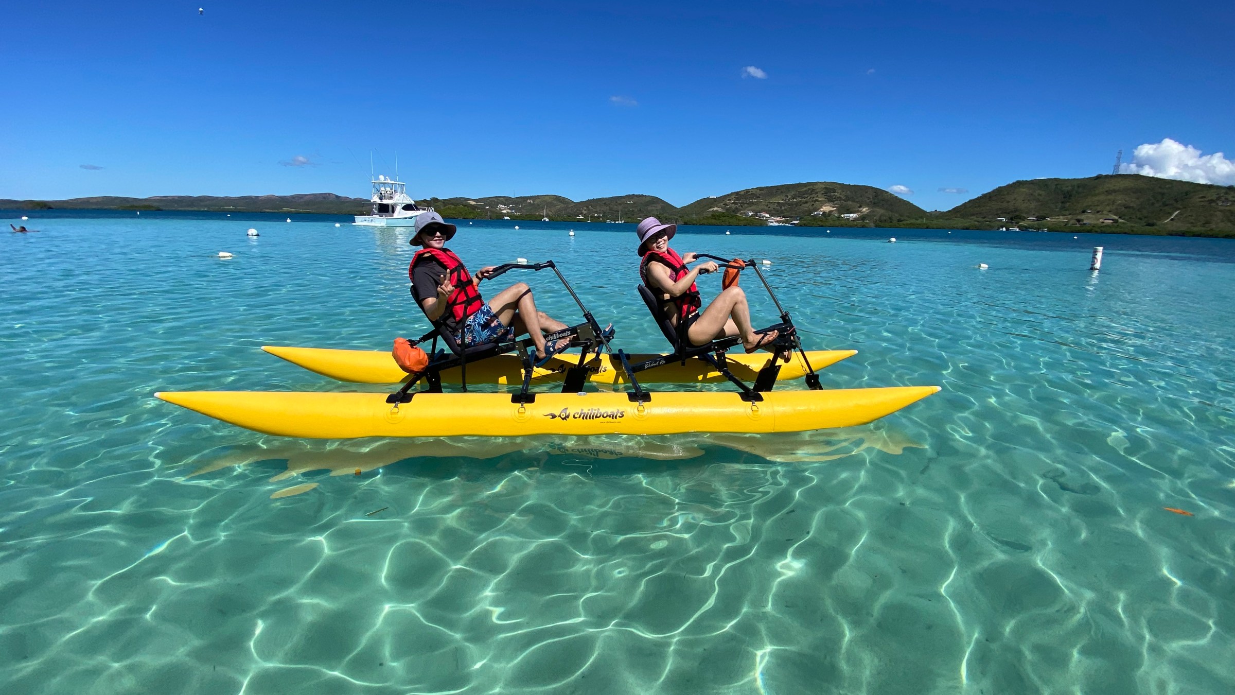 Two people riding a yellow water bike on clear blue ocean under a sunny sky.