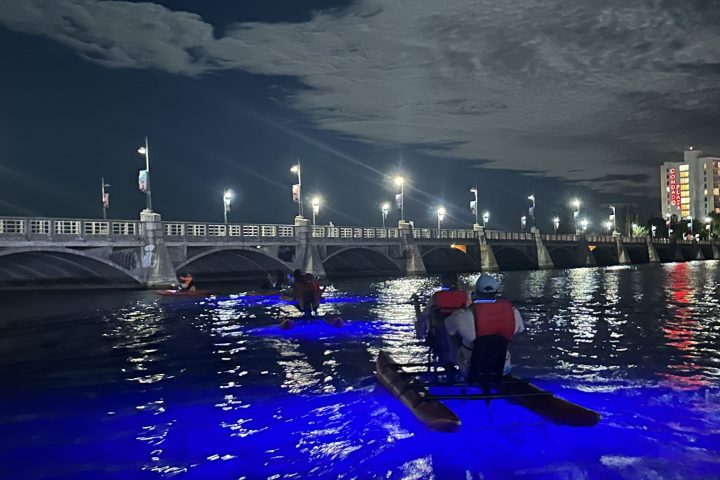 People kayaking at night with blue LED lights under a cloudy sky and moon.