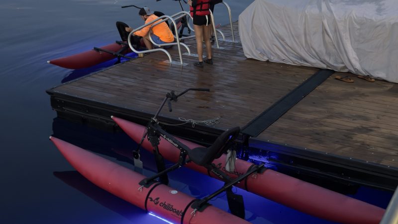 Two people preparing to board a kayak with red pontoons on a dock at a marina during dusk.
