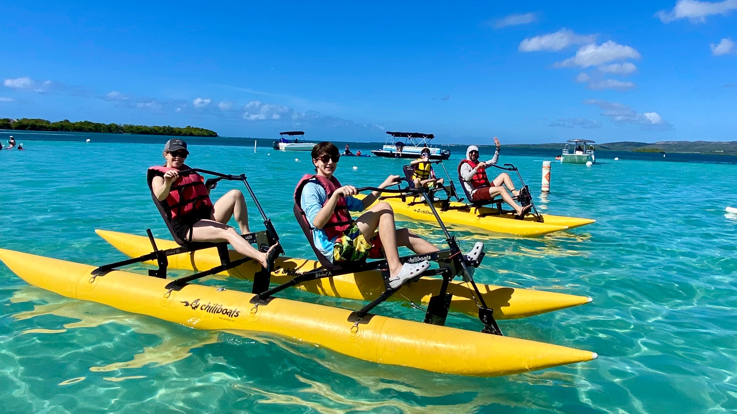 People on yellow water bikes in clear blue water under a bright blue sky.