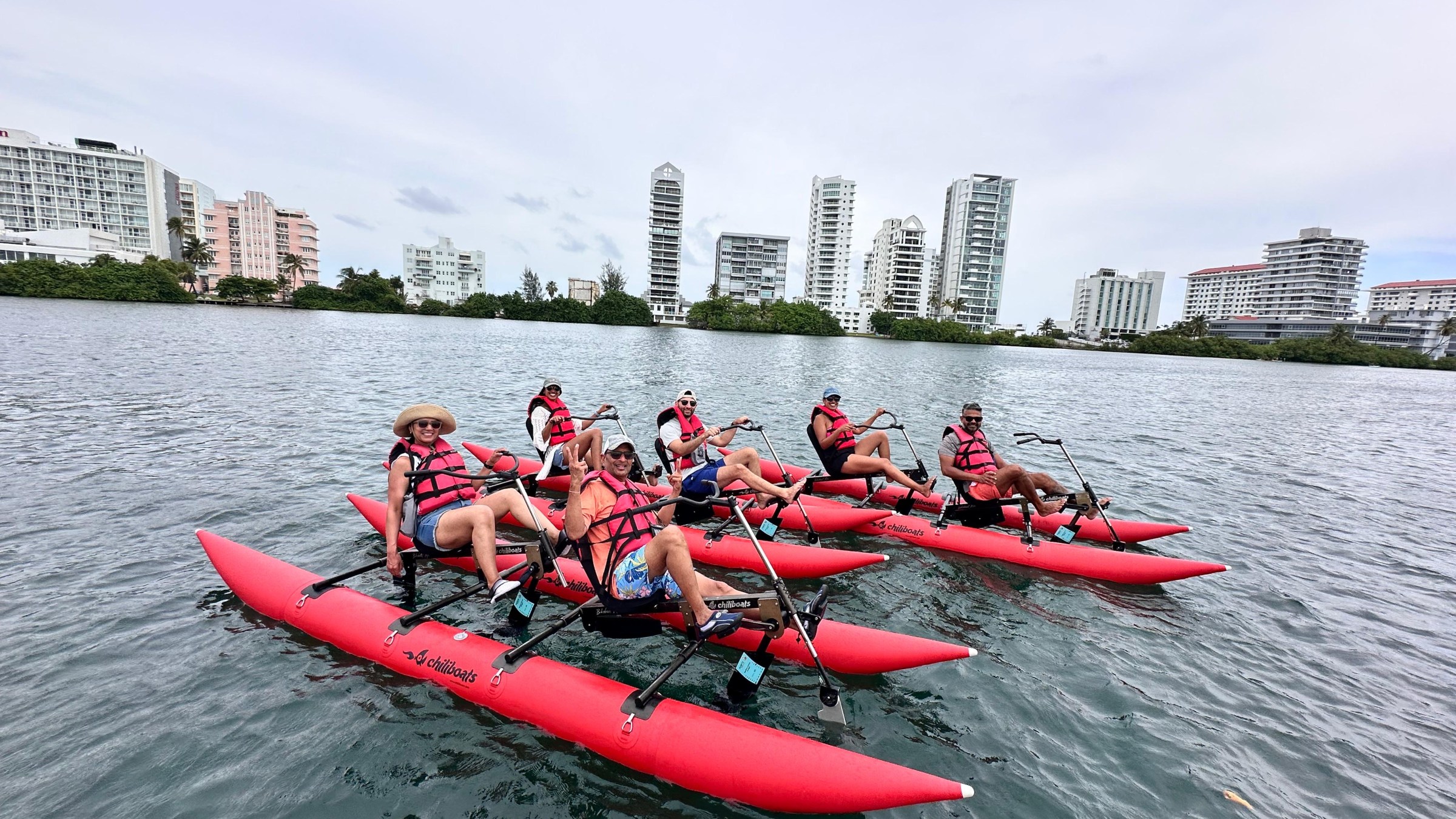 Group of people on red water bikes in a bay, city buildings in background.
