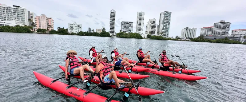 Group of people on red water bikes in a bay, city buildings in background.