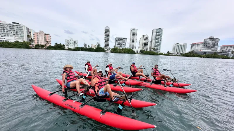 Group of people on red water bikes in a bay, city buildings in background.