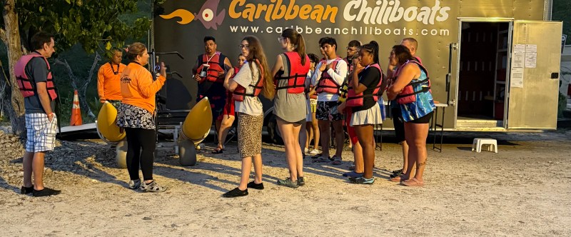 Group of people in life vests gather around a trailer labeled 'Caribbean Chillboats' with an instructor.