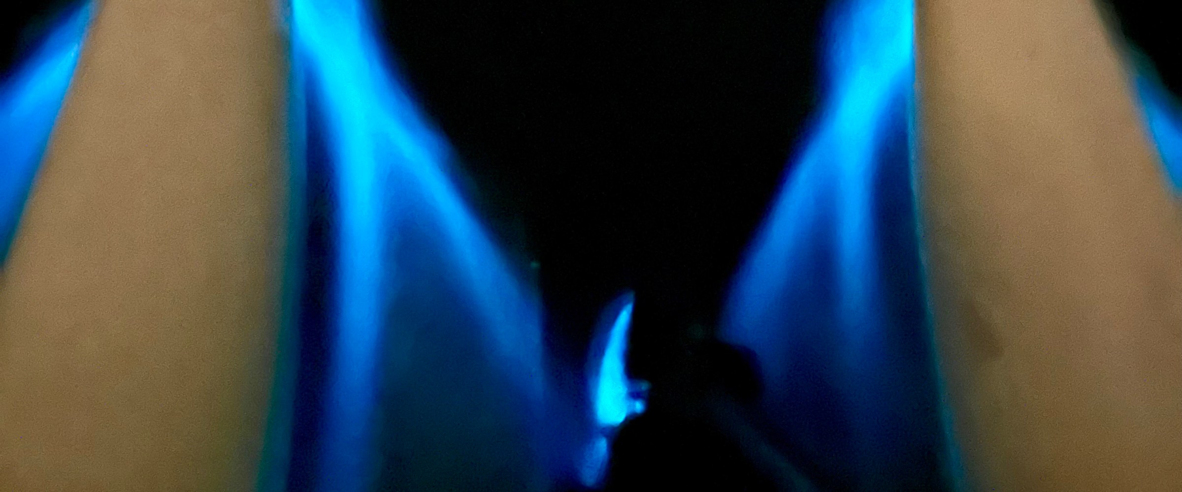 Blue flames between two dark triangular shapes at night.