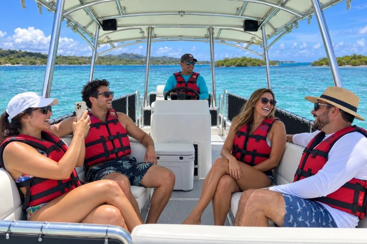Five people in life vests on a boat enjoying a sunny day on the water.