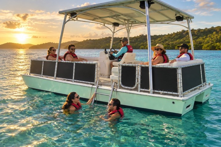 People on a pontoon boat and swimming in clear water at sunset.