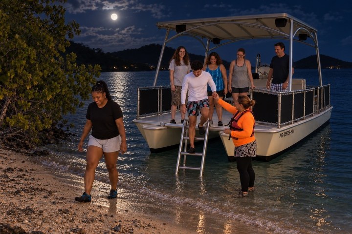 Group disembarking a boat onto a moonlit beach at night.