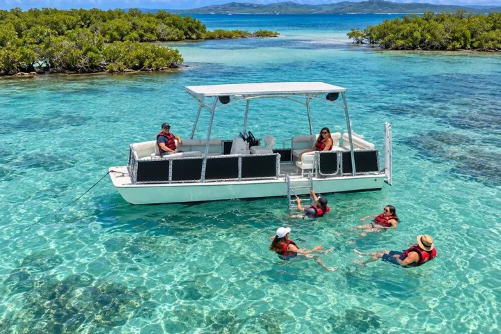 People swimming near a boat in clear turquoise water with mangrove islands in the background.