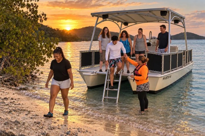 People disembarking a boat onto a beach at sunset.