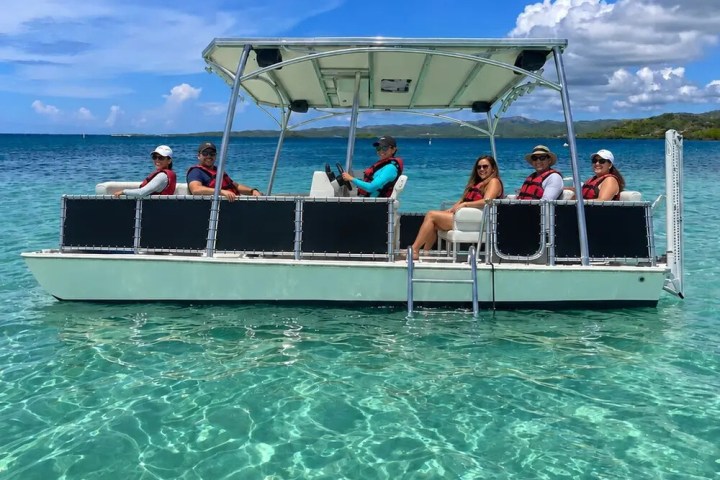 People on a pontoon boat in clear turquoise water under a partly cloudy sky.
