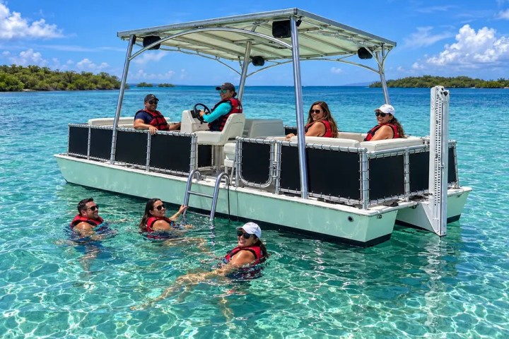 People on and around a boat in clear blue water, wearing life vests.